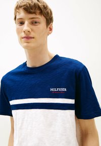 Camiseta de rayas navy y blanca con cuello redondo. Presenta el logo "HILFIGER" en hilo blanco y rojo en el pecho. Material de mezcla de algodón.