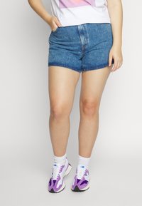 Pantalones cortos de mezclilla con dobladillo sin terminar, color azul claro, diseño de cinco bolsillos y un corte relajado. Combinados con calcetines blancos y zapatillas con acentos morados.