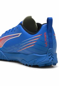 Chaussure de sport bleue avec des rayures orange et blanches, semelle texturée, col rembourré, et le texte "ULTRA" près du talon.