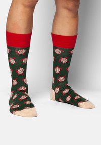 Grüne Socken mit roten Bündchen, die mit Schildkrötenmustern in Weiß und Rot verziert sind. Weicher Stoff, Knöchellang und mit einem beigen Zehenbereich.