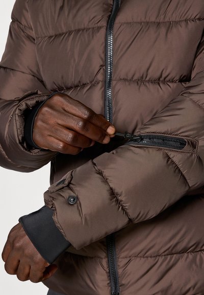 Braune Pufferjacke mit Stepptextur, ausgestattet mit einer Reißverschlusstasche am Arm und elastischen Bündchen für einen engen Sitz.