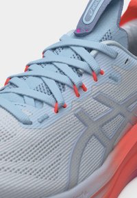 Light blue Asics running shoe with coral accents, laces threaded through red eyelets, and breathable mesh upper.