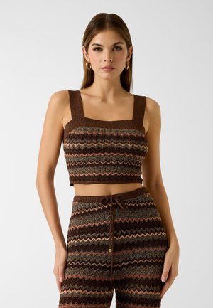 Femme portant un crop top en maille à motifs zigzag marron, rose et orange avec des bretelles larges, assorti à un pantalon taille haute à cordon de serrage.
