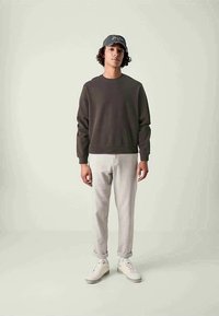 Sweatshirt cinza escuro de gola redonda, calças cinza claro ajustadas, ténis brancos. Modelo está de pé contra um fundo claro, usando um boné cinza.