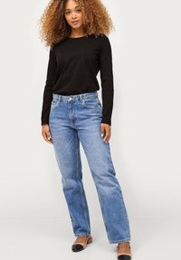 Zwarte longsleeve shirt gecombineerd met lichtblauwe high-waisted straight-leg jeans. De jeans hebben vijf zakken en riemlussen. Zwarte flats maken de look af.