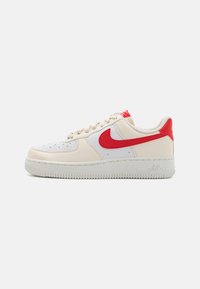 Scarpe Nike Air Force 1, con una tomaia in pelle bianca e dettagli beige, marchio rosso, tessuto testurizzato e suola in gomma.