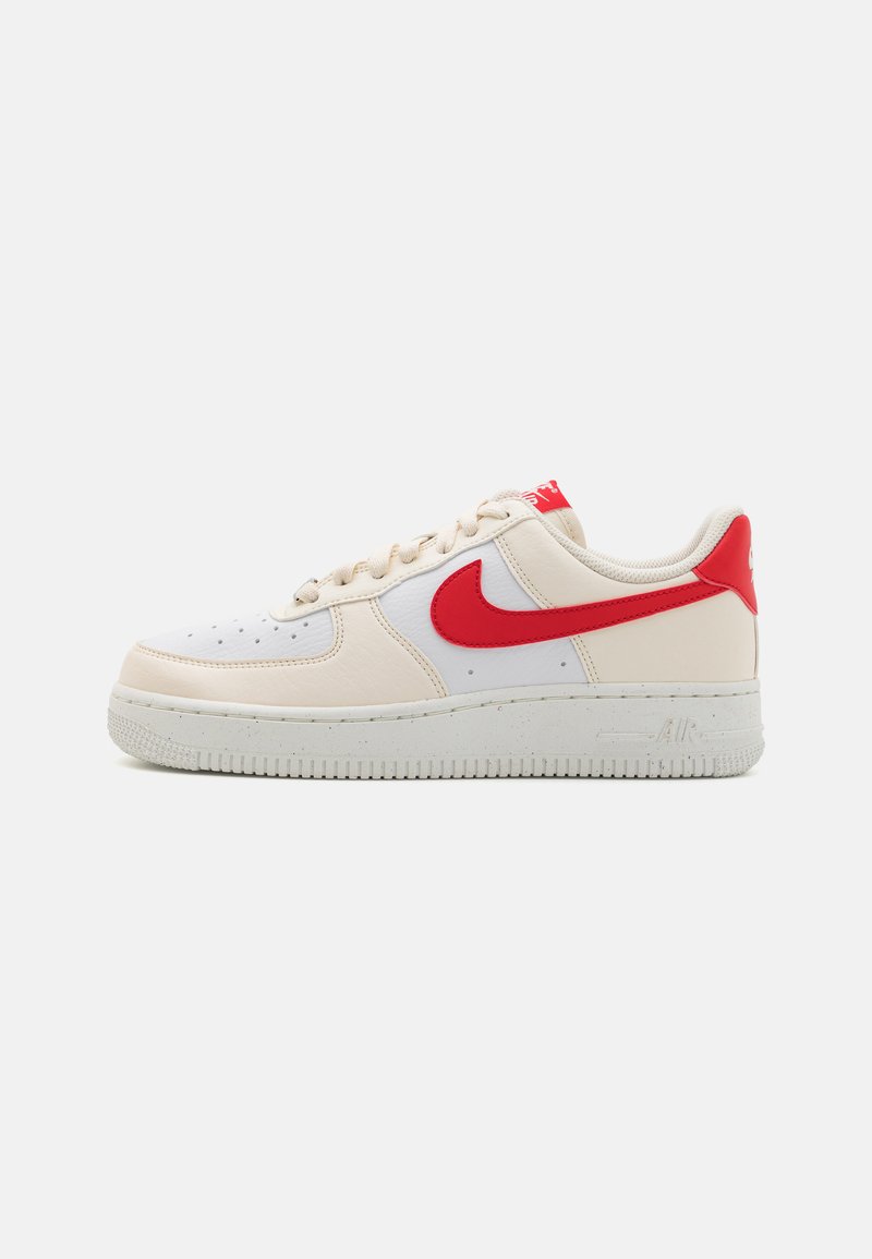 Scarpe Nike Air Force 1, con una tomaia in pelle bianca e dettagli beige, marchio rosso, tessuto testurizzato e suola in gomma.