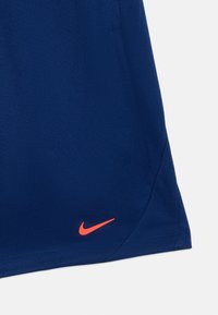 Pantalones cortos deportivos azul real hechos de una tela ligera, con un pequeño logo de Nike en naranja en el dobladillo inferior izquierdo.