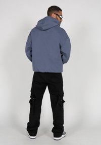 Hooded sweatshirt in slate gray with a relaxed fit, paired with black cargo pants featuring multiple pockets and ties, worn with black sneakers.