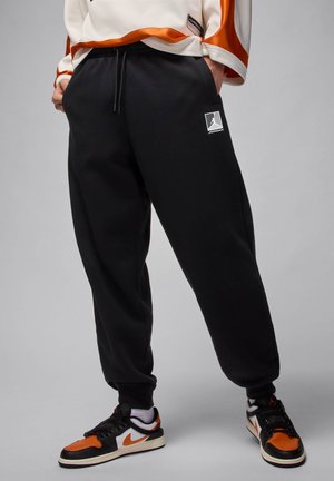 Sorte sweatpants med en afslappet pasform, der har en snoretræk i taljen og et hvidt logo patch. Sammen med multikolorede sneakers.