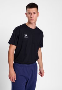 Zwarte korte mouwen T-shirt van katoen met een ronde hals. Kenmerkend is het witte "hummel" logo op de linkerkant van de borst. Gemaakt met marineblauwe broek.