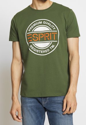T-shirt en coton vert olive avec un logo circulaire blanc et orange comportant du texte. Manches courtes et design classique à col rond.