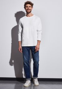 Camisa blanca de manga larga, jeans azules y zapatillas blancas. Ajuste casual, material de algodón, diseño simple con un logo sutil en el pecho.