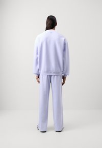 Lavandas izmēra džemperis un saskaņotas bikses no mīksta auduma. Brīvi pieguļošs stils ar nolaidām plecu šuvēm un elastīgu aprocēm. Vienkāršs, bez rotājumiem dizains.