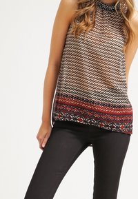 Haut sans manches à motifs beige et marine, avec des dessins géométriques et une bordure colorée. Le tissu semble léger avec une finition texturée.