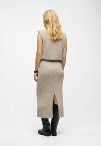 Robe en tricot beige avec une finition texturée, dotée d'un corsage ajusté, d'une jupe longue avec une fente dans le dos, portée avec des bottes noires jusqu'aux genoux.