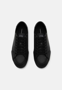 Zapatillas sintéticas negras con textura suave, con cordones planos negros y una lengüeta con marca. Punta redondeada y diseño minimalista.
