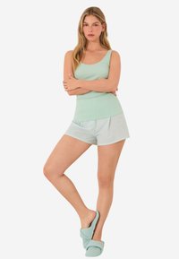 Débardeur côtelé vert clair associé à un short à motifs. La modèle porte des chaussons assortis en vert menthe, avec un tissu doux et texturé.