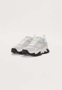 Scarpe sportive di un colore beige chiaro, realizzate in mesh, pelle e gomma; suola spessa bianca con accenti neri; lacci rotondi e linguetta per il trasporto.