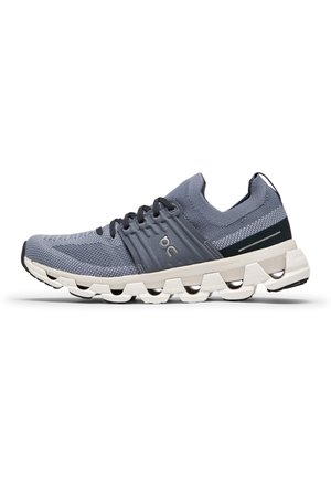 Sportlicher Schnürschuh mit grauem Mesh-Obermaterial, gepolsteter weißer Sohle und schwarzen Akzenten. Mit Logo an der Seite und strukturiertem Muster.
