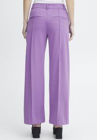 Pantalons à jambes larges en tissu violet vif, avec une texture lisse, des poches arrière bien taillées et un design taille haute. Talons plats noirs visibles.