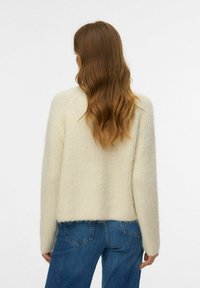 Krämfärgad tröja med strukturerad stickning, med avslappnad passform och sänka axlar, parat med blå denimjeans.