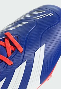 Scarpino da calcio blu con superficie texturizzata, dotato di lacci rossi e strisce bianche prominenti. Progettato per prestazioni e stabilità.