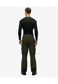 Zwarte langemouwen compressietop gecombineerd met olijfgroene cargobroek met zakken en een zwarte zoom, gedragen met zwarte laarzen.