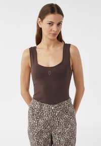 Brauner gerippter Body mit square Ausschnitt, kombiniert mit beigen Hosen, die ein dunkelbraunes Leopardenmuster aufweisen.