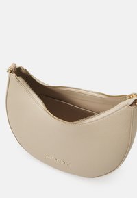 Beige läderhandväska med en böjd form, som har en dragkedja upptill och guldfärgad hårdvara. Varumärket "Valentino" är präglat framtill.