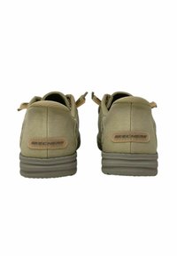 Zapatos Skechers en lona verde oliva con superficie texturizada, que cuentan con una suela acolchada y un acento de logo beige en el talón.