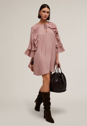 Abito rosa fluente con maniche arruffate, scollatura a chiave e cordoncino. Abbinato a stivali marrone scuro morbidi e una borsa nera.
