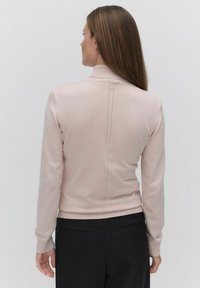 Lichtroze, aansluitende trui met lange mouwen en een hoge kraag. Beschikt over een achterkantnaad met een decoratieve knop. Zachte, gebreide textuur.