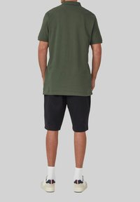 Olijfgroene polo met korte mouwen, gemaakt van katoen, met een rechte zoom. Gepaard met zwarte shorts, witte enkelsokken en beige sneakers.