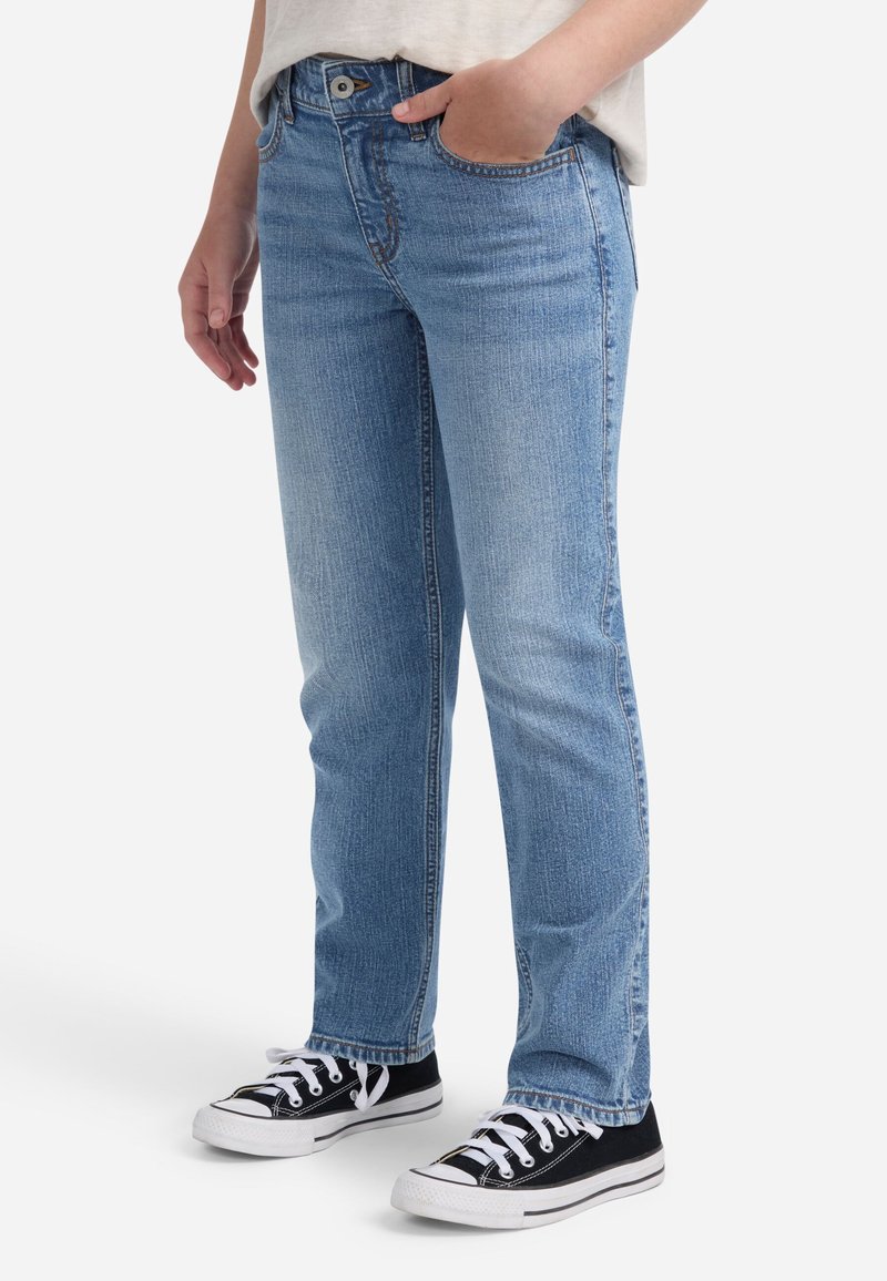 Svijetloplave traperice ravnog kroja, s klasičnim dizajnom s pet džepova i suptilnom izblijedjelom teksturom, uparene s crnim tenisicama.