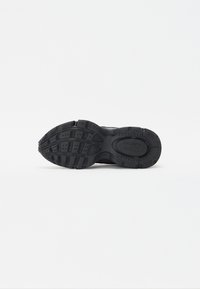 Svart såle på sneakers med gummimateriale, teksturerte grep mønstre og en fremtredende logo. Bøyd form med variert mønster for godt feste.