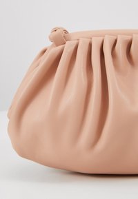 Pink faux leather handbag with gathered texture, rounded shape, and knot detail at the top, showcasing a smooth and glossy finish.