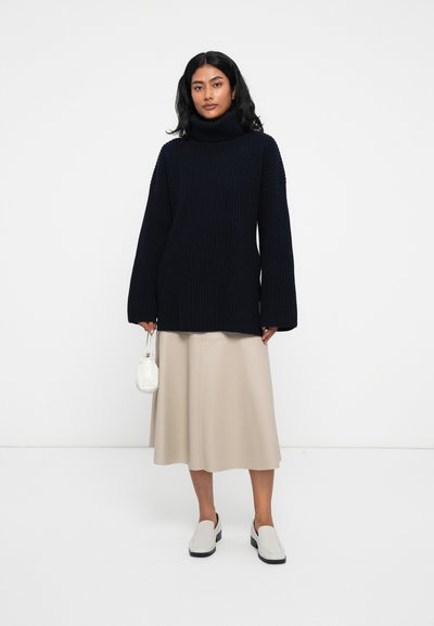Mornarsko modra rebrasta turtleneck pulover s dolgimi rokavi, v kombinaciji s bež A-linijo krila in belimi loaferji. Nosila je majhno belo torbico.