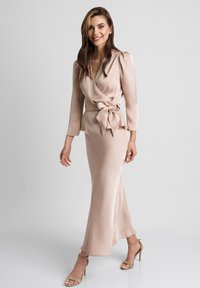 Nude satenowa długa sukienka z wiązaniem w talii, z długimi rękawami i zwiewnym dołem. Para sandałków na paski.