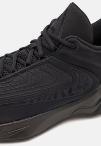Chaussure de sport noire avec tige en tissu texturé, col rembourré, coutures détaillées et lacets noirs sur une semelle épaisse.