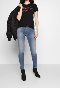 Svart T-shirt med röd grafisk tryck, ihopparad med ljusblå skinny jeans med sidofickor, och svarta klackade ankelstövlar.