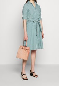 Abito a righe verde e bianco, con colletto a bottoni, maniche corte e vita annodata. Porta una piccola borsa a secchiello color rosa pallido.