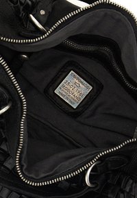 Interno di borsa in pelle nera, con etichetta riportante dettagli del marchio e della produzione. Foderata con tessuto liscio, chiusura con zip metallica e dettagli intrecciati.