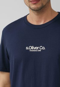 Navyblauwe katoenen T-shirt met korte mouwen, met een witte logo "s.Oliver Co. Opgericht 1969" op de borst. Zachte textuur.