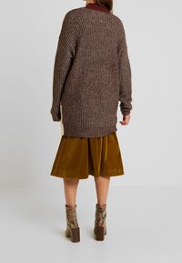 Ruskea neulotulla neuletakilla, jossa on rento istuvuus ja teksturoitu pinta. Yhdistetty sinapinväriseen samettihameeseen ja käärmeennahkavarrellisiin nilkkabootseihin, joissa on paksut korot.