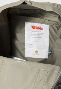 Vihreä kangasvuori, jossa valkoinen etiketti, jossa lukee "Fjällräven." Sisältää sinivalkoisen Ruotsin lipun ja näkyvät ompelukuvioinnit.