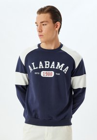 Navy Sweatshirt mit cremefarbenen Raglanärmeln. Mit der Aufschrift "ALABAMA SOUTH 1988 TEAM" in weißem Text. Gerippter Kragen und Saum, weicher Stoff.