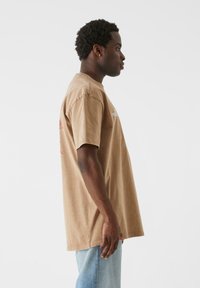 Brown cotton t-shirt with short sleeves and a relaxed fit, featuring minimalistic graphics in white and red on the front and back.