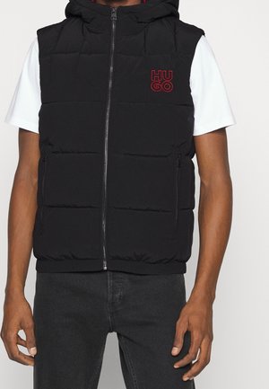 Schwarze gesteppte ärmellose Kapuzenweste mit Frontreißverschluss und rotem "HUGO"-Logo, getragen über einem weißen Kurzarmshirt.