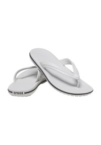 Tongs blanches en plastique léger avec un semelle texturée, des fines lanières et une ligne d'accent noir sur la semelle, arborant le logo "crocs".